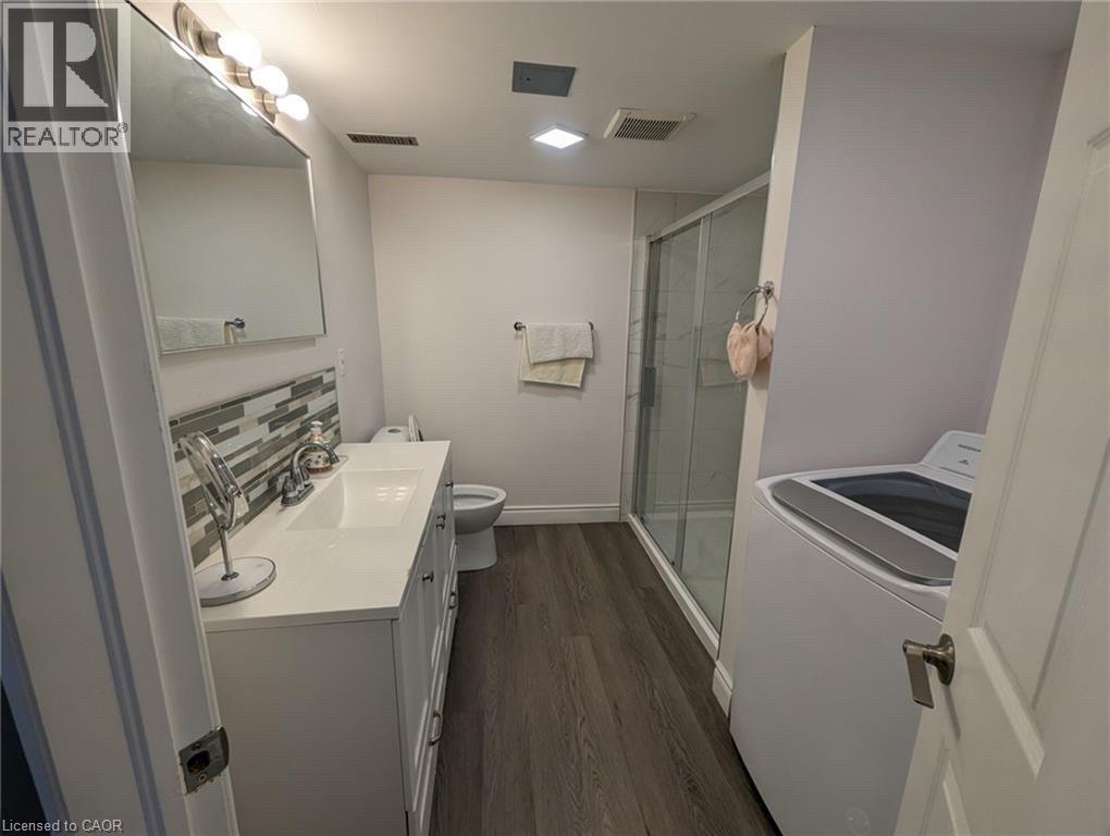 Spacious bathroom featuring a white vanity with integrated sink, glass-enclosed shower, wood-finish flooring, and a modern top-load washer - 510 Oakridge Place, Waterloo, ON - Indoor Photo Showing Laundry Room