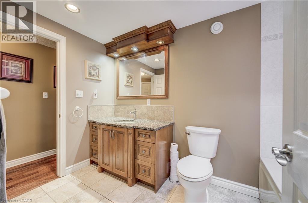 Bathroom featuring a wood-finish vanity with granite-style countertop, integrated sink, and brushed nickel faucet - 599 Coldstream Drive, Waterloo, ON - Indoor Photo Showing Bathroom