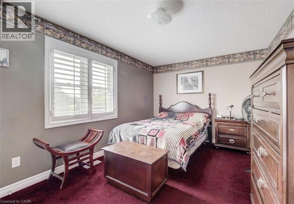 Bedroom featuring a window with white louvered shutters, textured wall covering, deep red carpeting, and a ceiling-mounted light fixture - 599 Coldstream Drive, Waterloo, ON - Indoor Photo Showing Bedroom