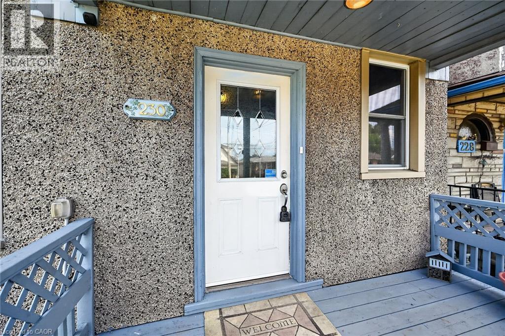 Front entry featuring a white door with decorative glass, a single window with light trim, a textured exterior, and a wooden porch with railing - 230 Picton Street E, Hamilton, ON - Outdoor With Exterior