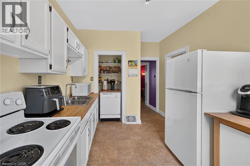 Kitchen featuring white cabinetry, wood-finish countertops, stainless steel sink, and tile flooring - 230 Picton Street E, Hamilton, ON - Indoor Photo Showing Kitchen With Double Sink