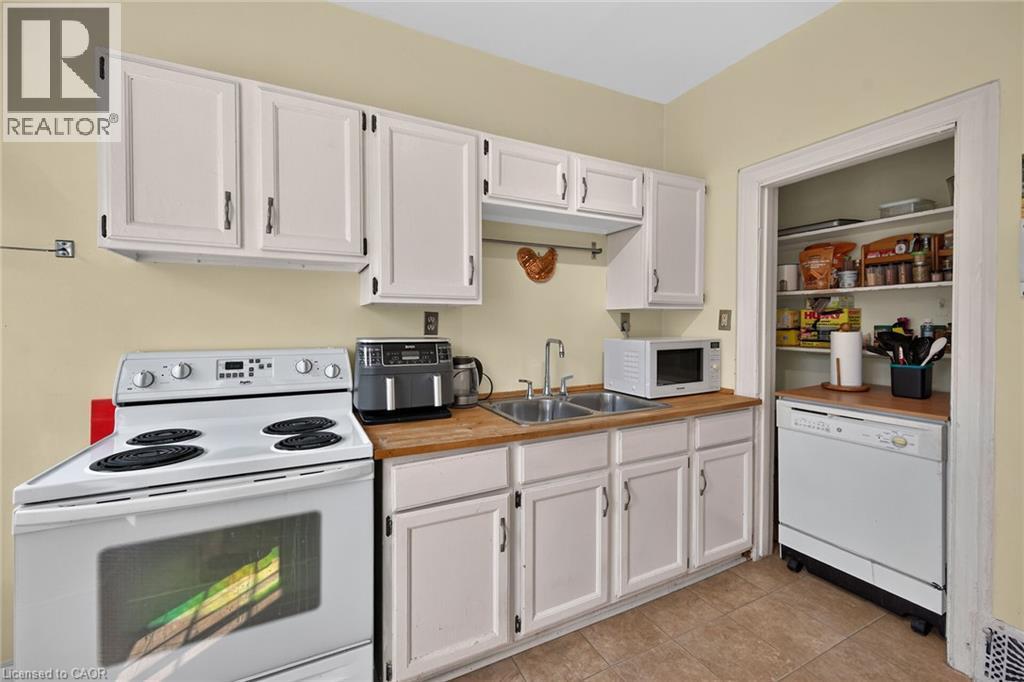 Kitchen featuring white cabinetry, wood-finish countertops, tile flooring, a dual-basin sink, and a built-in pantry with shelving - 230 Picton Street E, Hamilton, ON - Indoor Photo Showing Kitchen With Double Sink