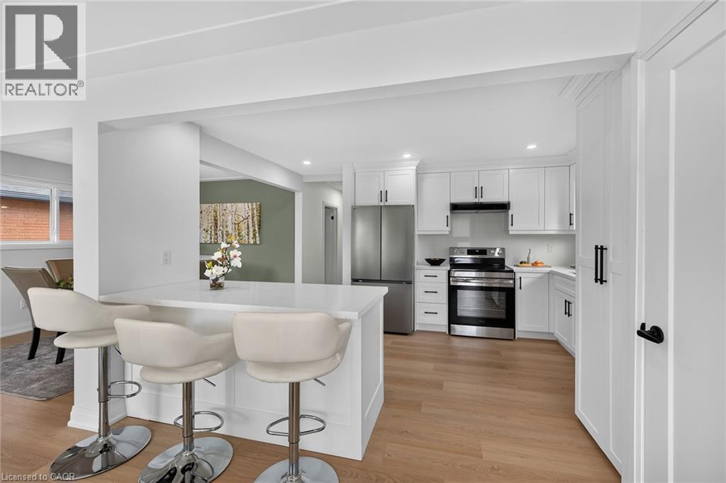 White shaker-style cabinetry with matte black hardware, stainless steel appliances, light wood-finish flooring, and a breakfast bar with a solid surface countertop - 40 Purdy Crescent, Hamilton, ON - Indoor