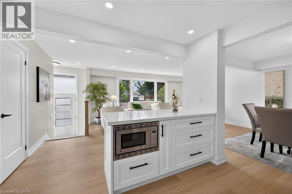 White kitchen island with a built-in microwave, light wood-finish flooring, recessed lighting, expansive windows, and a doorway with frosted glass panels - 40 Purdy Crescent, Hamilton, ON - Indoor