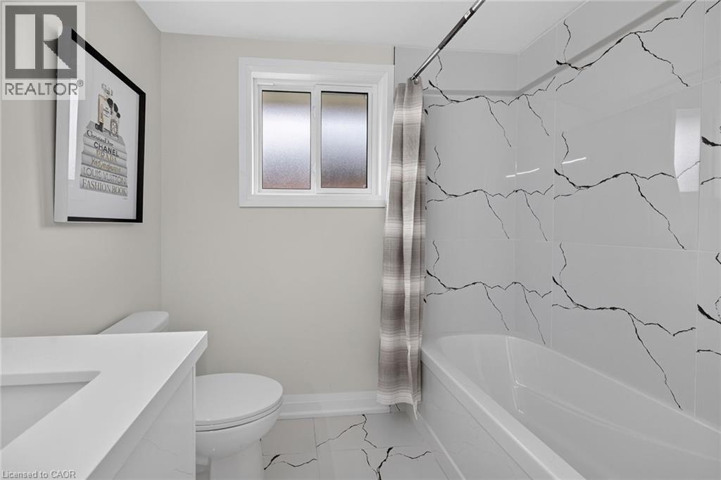 Crisp white bathtub with floor-to-ceiling accent tile, single vanity with integrated sink, and a white toilet - 40 Purdy Crescent, Hamilton, ON - Indoor Photo Showing Bathroom