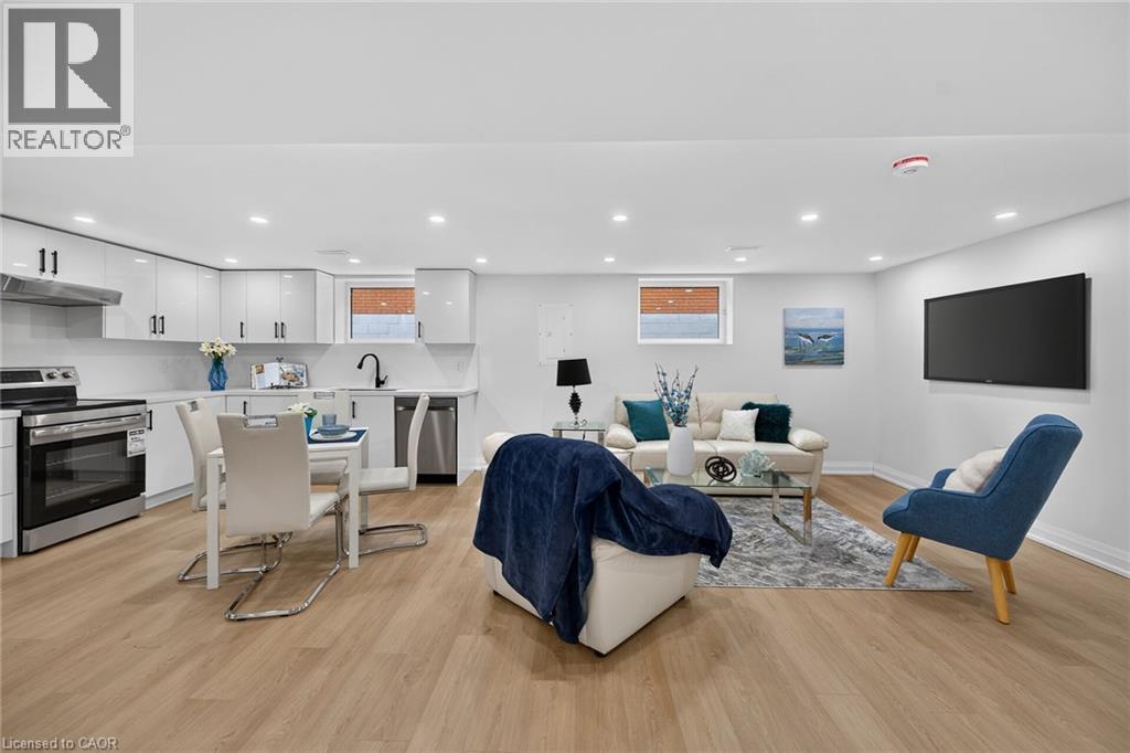 Open-concept living area featuring a kitchen with white cabinetry and stainless steel appliances, wood-finish flooring, recessed lighting, and a wall-mounted display - 40 Purdy Crescent, Hamilton, ON - Indoor