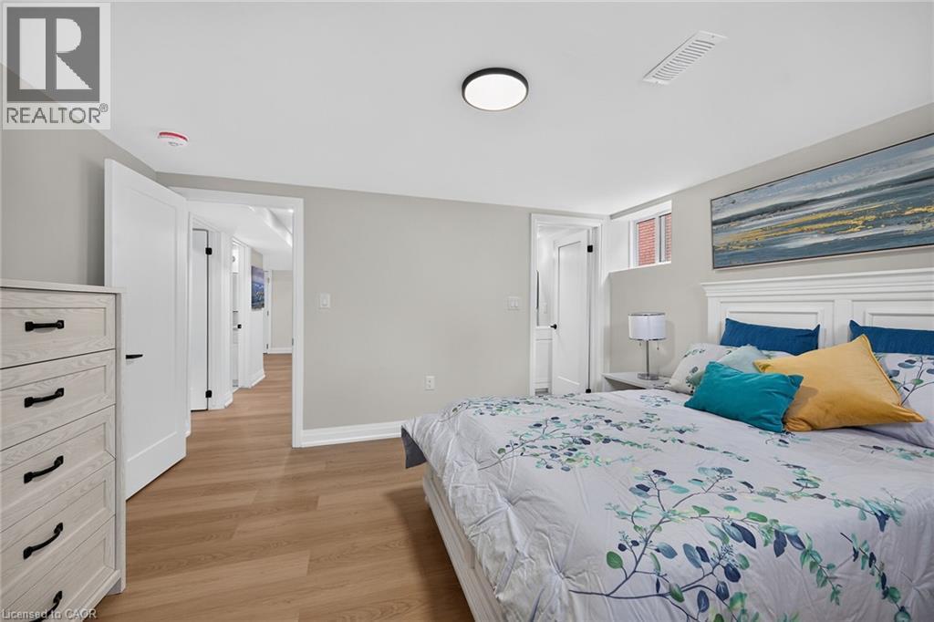 Light wood-finish flooring, white paneled doors with dark hardware, and a window with brick exterior visibility - 40 Purdy Crescent, Hamilton, ON - Indoor Photo Showing Bedroom