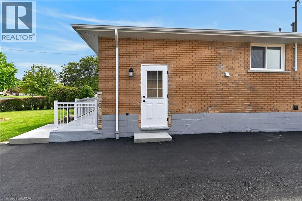 Brick exterior with white door, aluminum railing, exterior lighting fixture, and paved surface - 40 Purdy Crescent, Hamilton, ON - Outdoor
