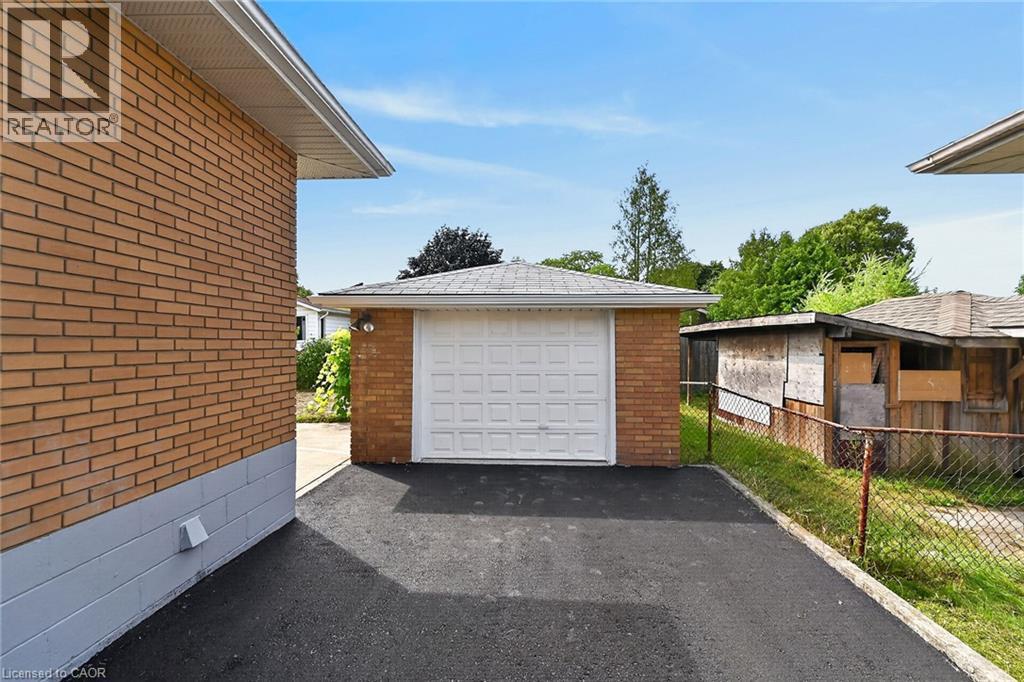 Detached brick garage with a panel-style door, asphalt driveway, and a chain-link property line - 40 Purdy Crescent, Hamilton, ON - Outdoor With Exterior