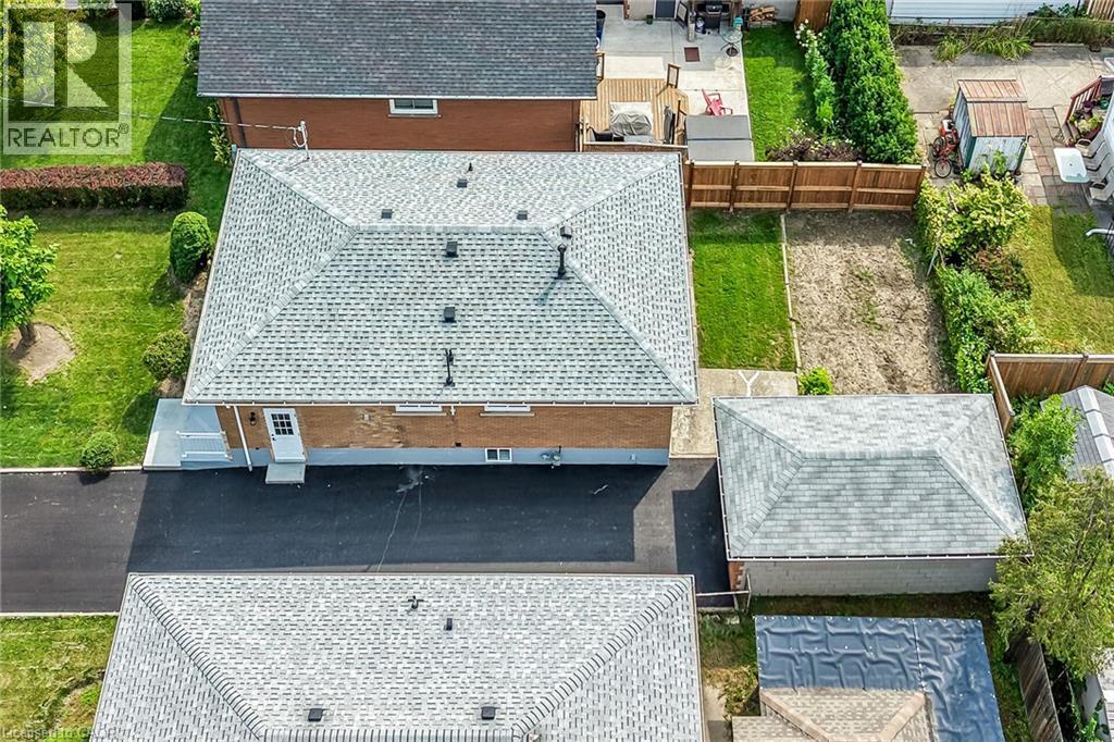 Expansive paved driveway leading to the property, pitched roof with asphalt shingles, mature trees and shrubs, brick exterior, and a wooden fence defining the property line - 40 Purdy Crescent, Hamilton, ON - Outdoor With Deck Patio Veranda