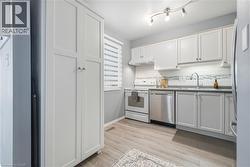 Kitchen featuring white cabinetry, stainless steel dishwasher, white range with coordinating range hood, and wood-finish flooring -