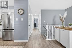Wood-finish flooring, white spindle railing, integrated white cabinetry with wood countertop, and stainless steel refrigerator -