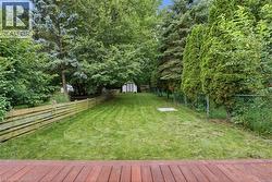 Expansive grassy yard enclosed by a wood-plank fence and a chain-link fence, featuring mature perimeter trees and a visible storage shed -