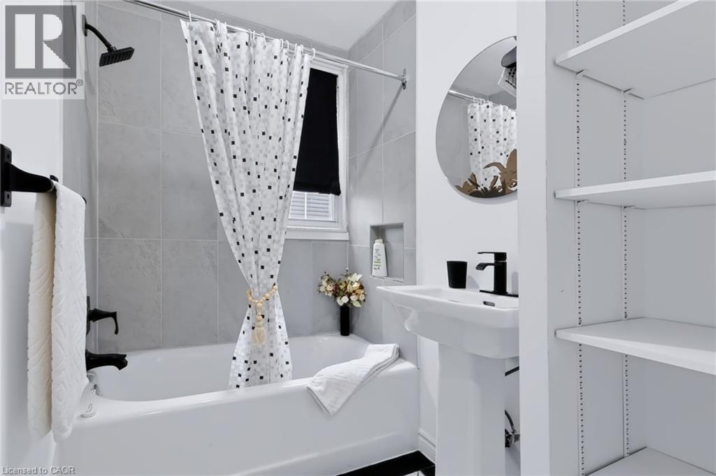 White bathtub with a matte black shower fixture, pedestal sink with a matte black faucet, and built-in shelving - 703 Brighton Avenue, Hamilton, ON - Indoor Photo Showing Bathroom