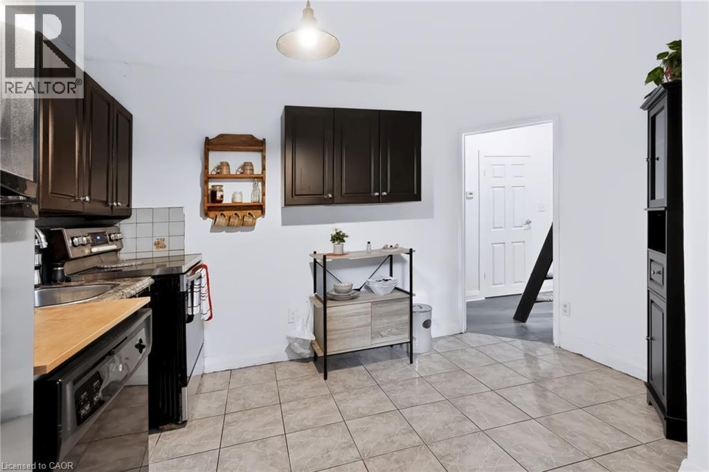 Kitchen featuring dark cabinetry, tile flooring, a built-in dishwasher, and a paneled door - 703 Brighton Avenue, Hamilton, ON