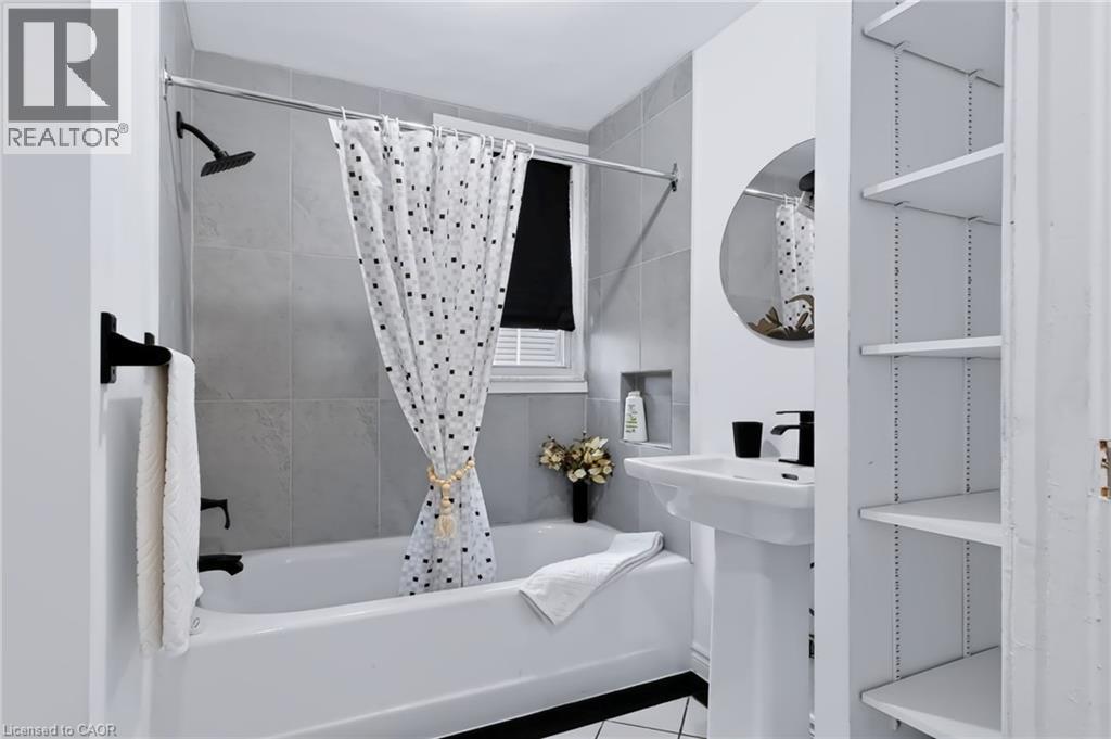 Full bathroom featuring a white porcelain pedestal sink, built-in shelving, and a tiled shower with a niche - 703 Brighton Avenue, Hamilton, ON