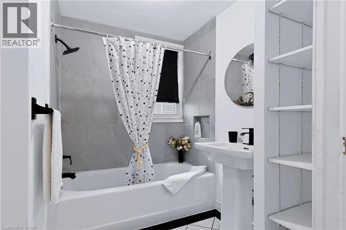 Full bathroom featuring a white porcelain pedestal sink, built-in shelving, and a tiled shower with a niche - 703 Brighton Avenue, Hamilton, ON 