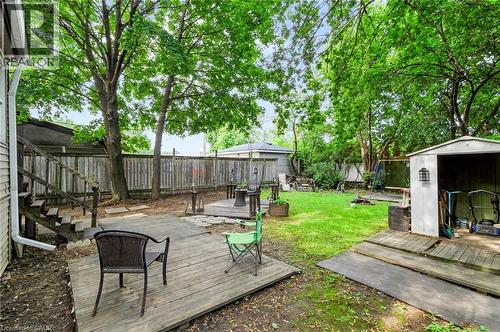 Expansive backyard featuring mature trees, a wooden privacy fence, a multi-level deck, a verdant lawn, and a storage shed - 703 Brighton Avenue, Hamilton, ON 