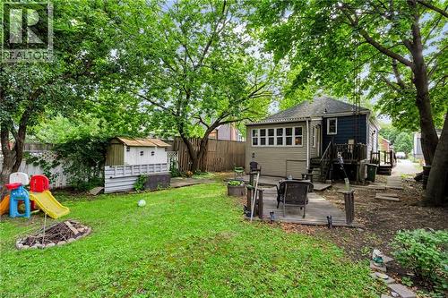 Expansive green yard with mature trees, a wooden privacy fence, a detached storage shed, a ground-level deck, and a fire pit area - 703 Brighton Avenue, Hamilton, ON 