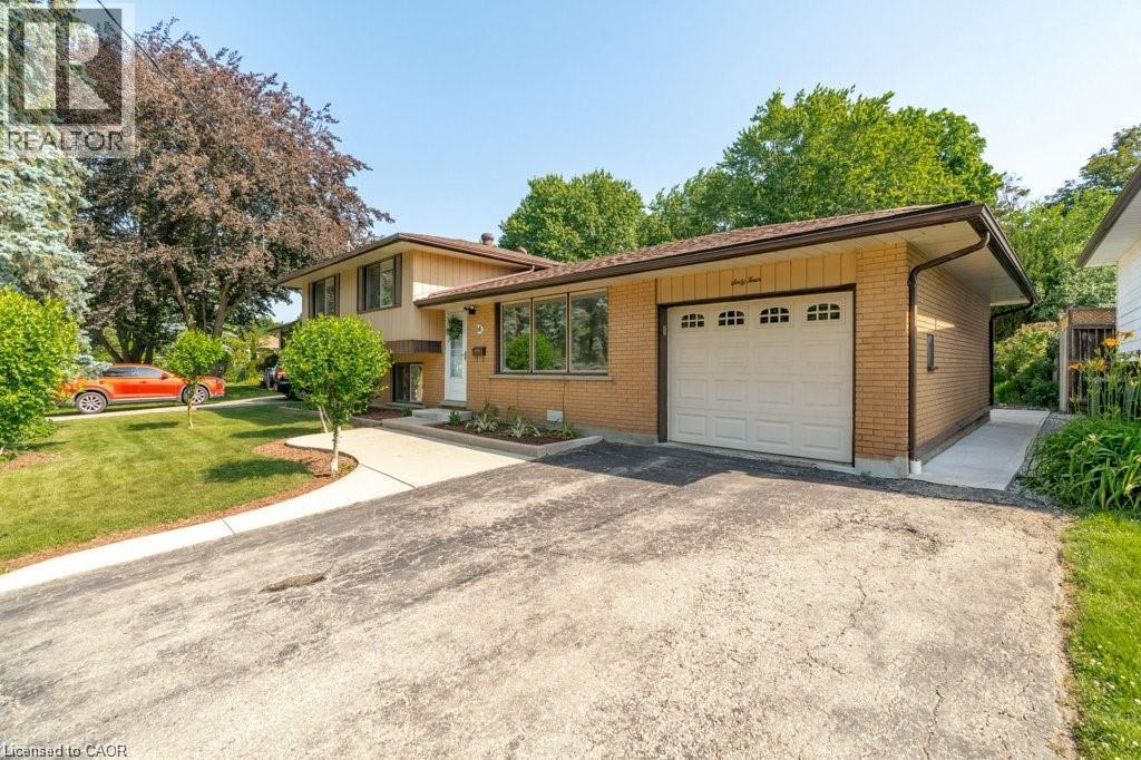 Brick-clad exterior with a garage, mature trees, and a concrete pathway leading to the entrance - 64 Warren Road, Kitchener, ON - Outdoor