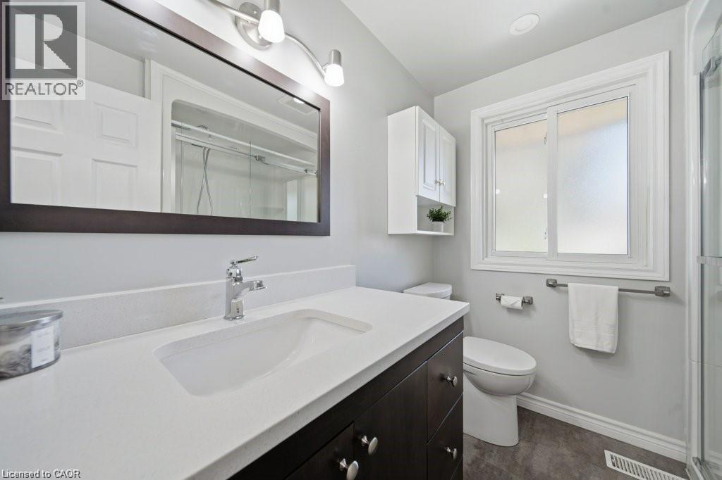 White vanity with integrated sink and chrome faucet, wood-finish flooring, and white-framed window - 64 Warren Road, Kitchener, ON - Indoor Photo Showing Bathroom