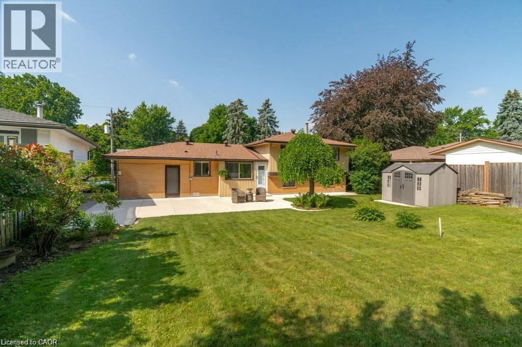 Expansive backyard featuring a manicured lawn, established perimeter fencing, concrete patio, and a detached storage shed - 64 Warren Road, Kitchener, ON - Outdoor