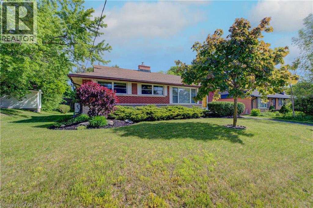 Red brick exterior with white trim, a brown shingle roof, front garden beds, mature trees, and a spacious green lawn - 251 Union Street E, Waterloo, ON - Outdoor