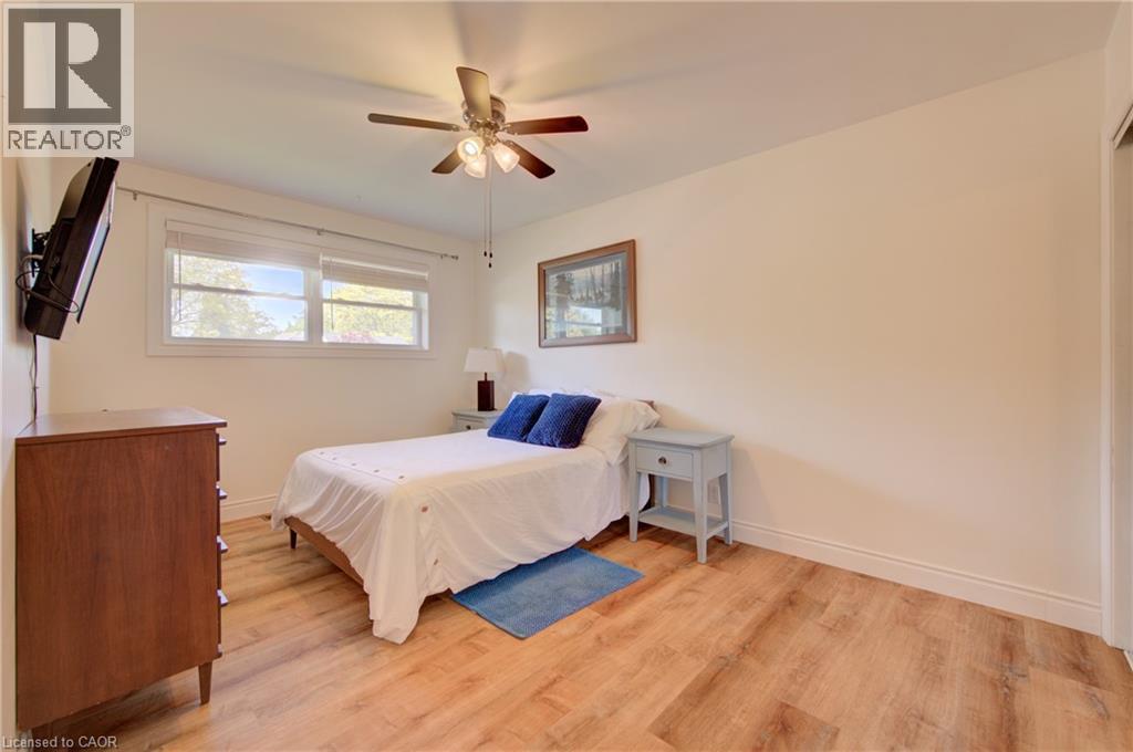 Wood-finish flooring with white baseboards, a ceiling fan with light fixture, and double windows with roller shades - 251 Union Street E, Waterloo, ON - Indoor Photo Showing Bedroom