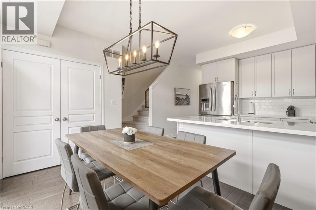 Open-concept dining and kitchen space featuring a modern chandelier, white flat-panel cabinetry, stainless steel appliances, and a white subway tile backsplash - 4171 Palermo Common, Burlington, ON - Indoor