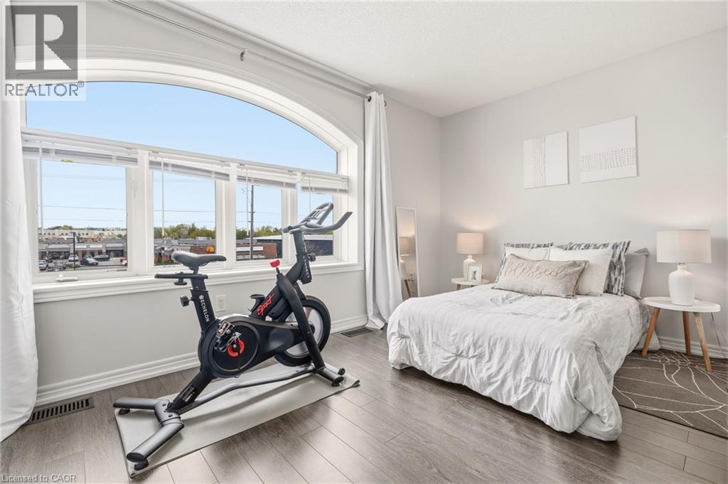 Expansive arched window with multiple panes, light gray wall paint, and wood-finish flooring - 4171 Palermo Common, Burlington, ON - Indoor Photo Showing Gym Room