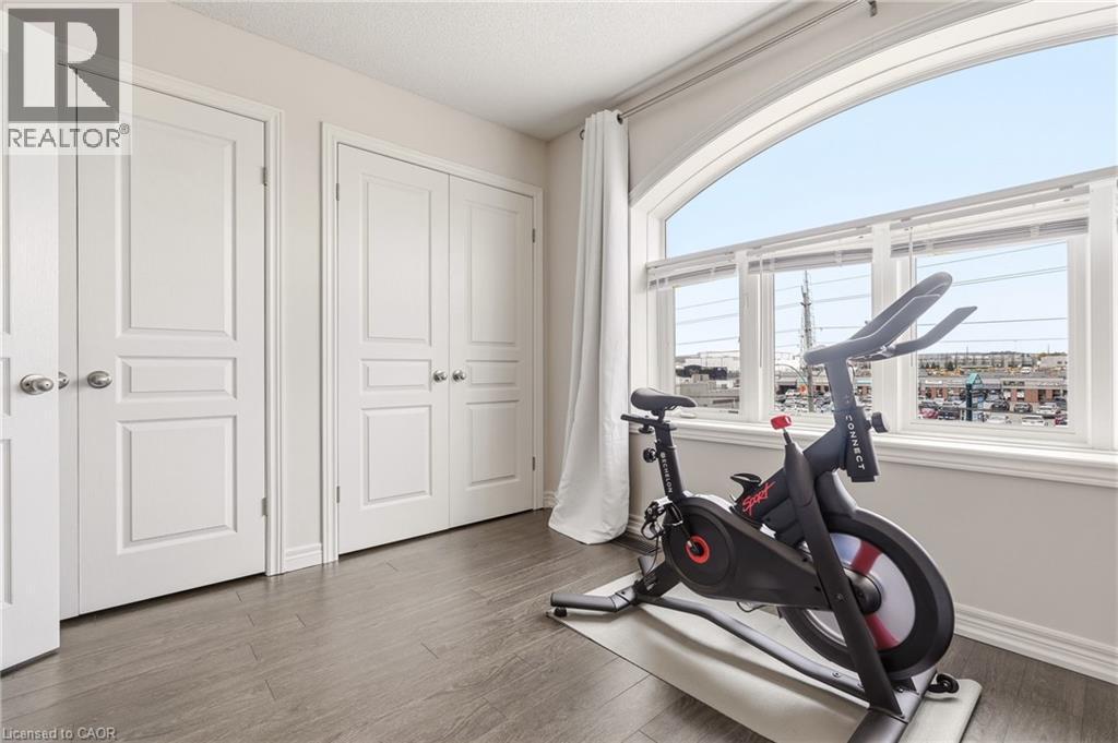 Bright corner bedroom showcasing expansive arched windows framing panoramic city vistas, rich wood-finish flooring, and crisp white six-panel closet doors with polished hardware - 4171 Palermo Common, Burlington, ON - Indoor Photo Showing Gym Room