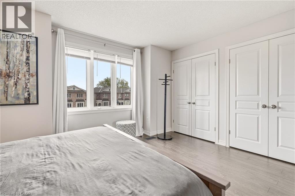 Large window with white trim, two sets of white double closet doors, and wood-finish flooring - 4171 Palermo Common, Burlington, ON - Indoor Photo Showing Bedroom