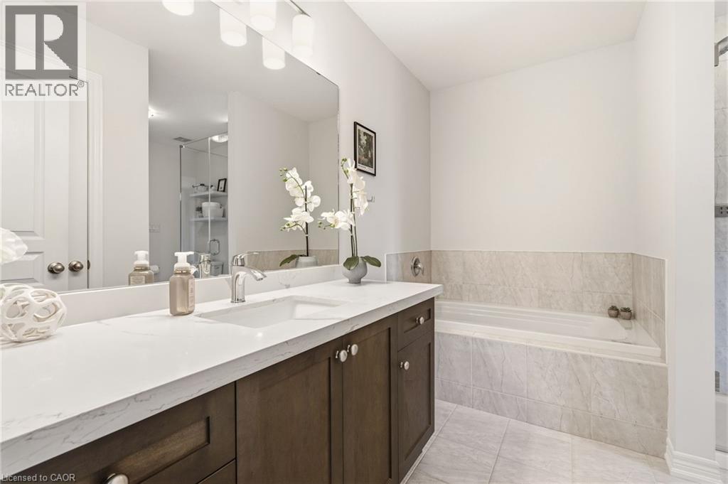 Integrated soaking tub, wood-finish vanity with ample storage, large rectangular mirror, and tiled flooring - 4171 Palermo Common, Burlington, ON - Indoor Photo Showing Bathroom