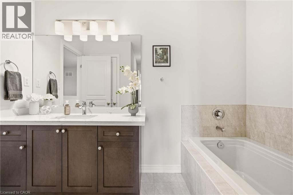 Spa-inspired primary bathroom featuring a dark wood vanity with dual sinks, marble-topped countertop, and large framed mirror with integrated lighting - 4171 Palermo Common, Burlington, ON - Indoor Photo Showing Bathroom