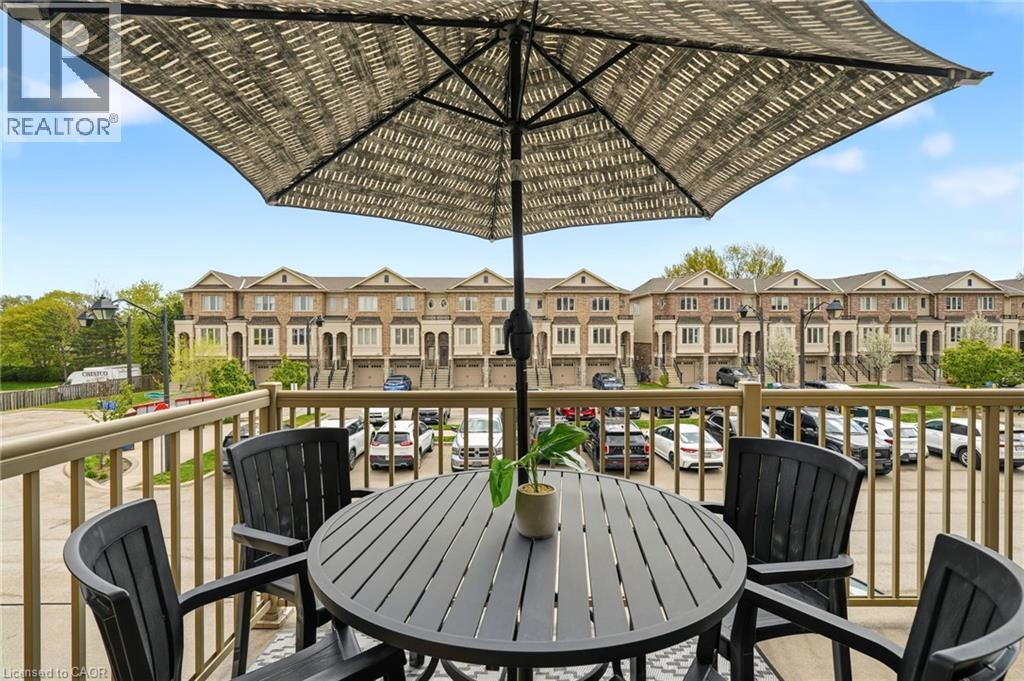 Elevated deck featuring a round wood-finish table, black Adirondack-style seating for four, and a large market umbrella with black pole - 4171 Palermo Common, Burlington, ON - Outdoor With Exterior