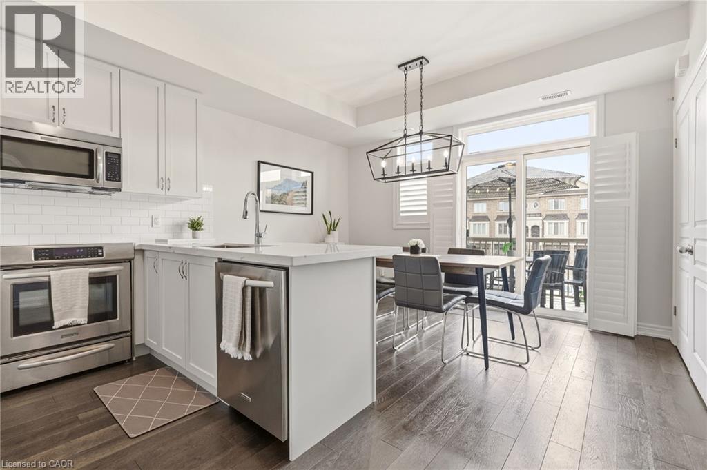Contemporary kitchen and dining area featuring white cabinetry with brushed metal hardware, stainless steel appliances including a double wall oven, quartz countertops, and a large waterfall-edge isla - 4171 Palermo Common, Burlington, ON - Indoor Photo Showing Kitchen