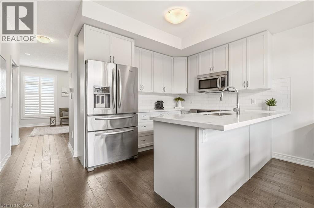 White shaker cabinetry, stainless steel appliances, white subway tile backsplash, white countertop, and wood-finish flooring - 4171 Palermo Common, Burlington, ON - Indoor Photo Showing Kitchen With Stainless Steel Kitchen With Upgraded Kitchen