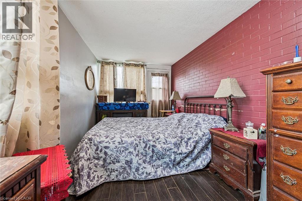 Dark wood-finish flooring, accent brick wall, and window with natural light - 27 Roseview Avenue, Cambridge, ON - Indoor Photo Showing Bedroom