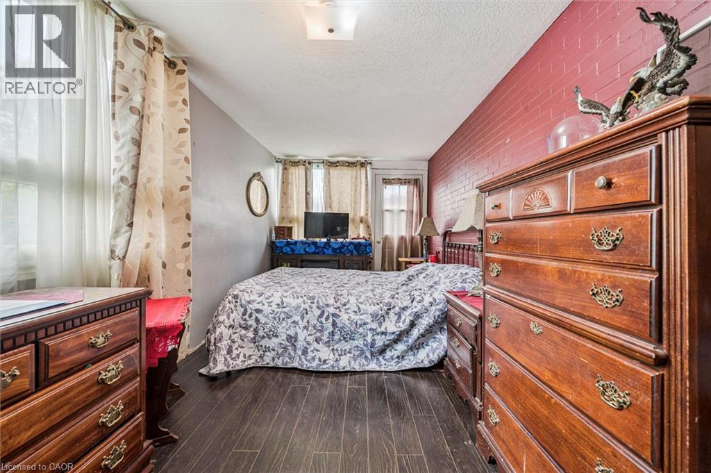 Brick accent wall, wood-finish flooring, and multiple windows - 27 Roseview Avenue, Cambridge, ON - Indoor Photo Showing Bedroom