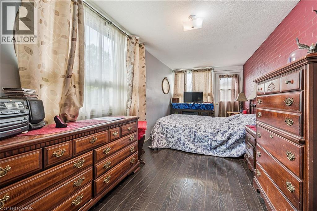 Wood-finish flooring with a contrasting brick-textured accent wall - 27 Roseview Avenue, Cambridge, ON - Indoor Photo Showing Bedroom
