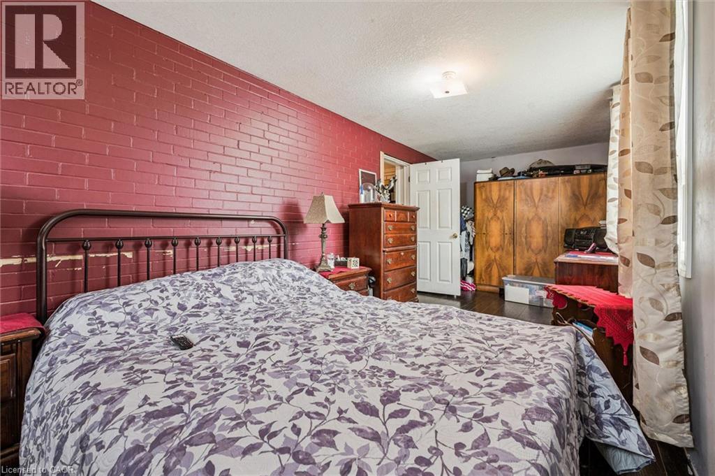 Brick accent wall, dark wood-finish flooring, white ceiling, white interior door - 27 Roseview Avenue, Cambridge, ON - Indoor Photo Showing Bedroom