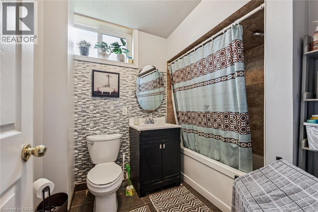 Bathroom featuring a tub/shower combination with tile surround, a single vanity with a round mirror, and a window for natural light - 27 Roseview Avenue, Cambridge, ON - Indoor Photo Showing Bathroom