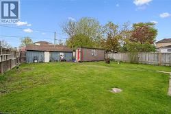 Expansive green lawn with a wooden privacy fence, featuring a large detached shed and an additional outdoor storage shed -
