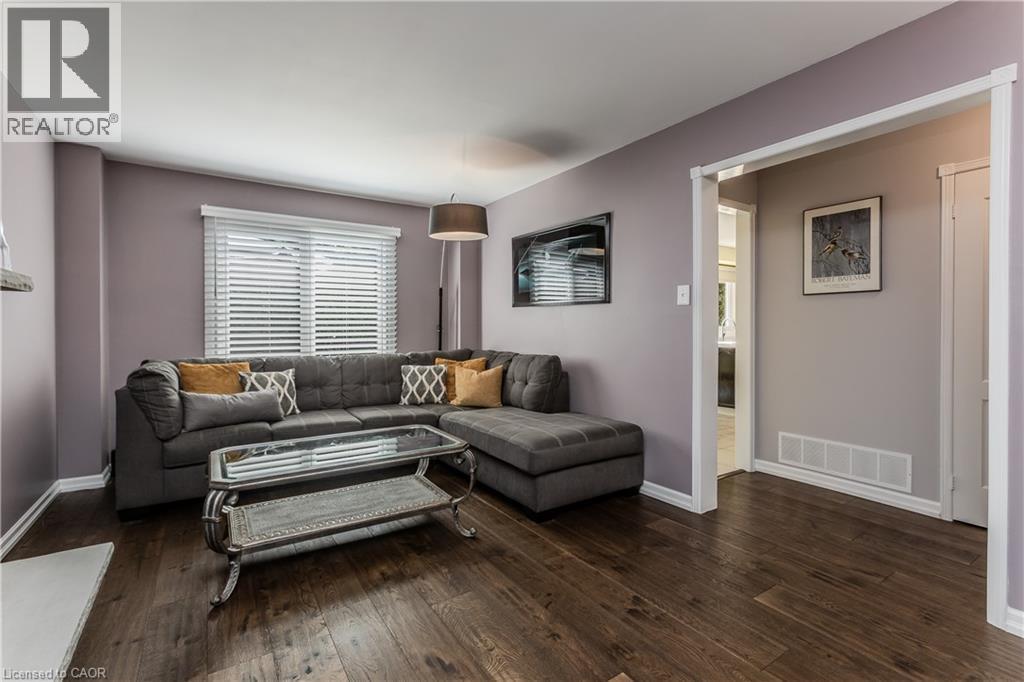 Wood-finish flooring throughout, featuring a window with horizontal blinds and a doorway with white trim - 1238 Sable Drive, Burlington, ON - Indoor Photo Showing Living Room