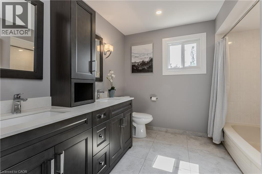 Dual vanity with integrated sinks, dark wood-finish cabinetry, and contemporary wall sconces - 1238 Sable Drive, Burlington, ON - Indoor Photo Showing Bathroom