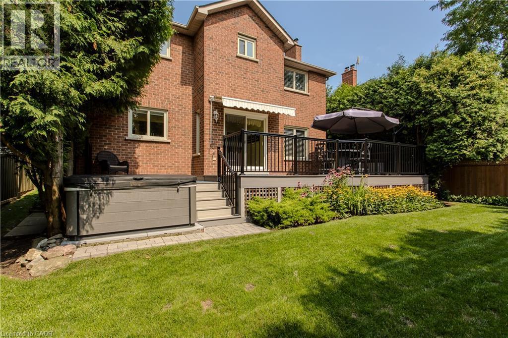Brick exterior featuring an elevated deck with black railings, a hot tub, and a manicured lawn with garden beds - 1238 Sable Drive, Burlington, ON - Outdoor With Deck Patio Veranda