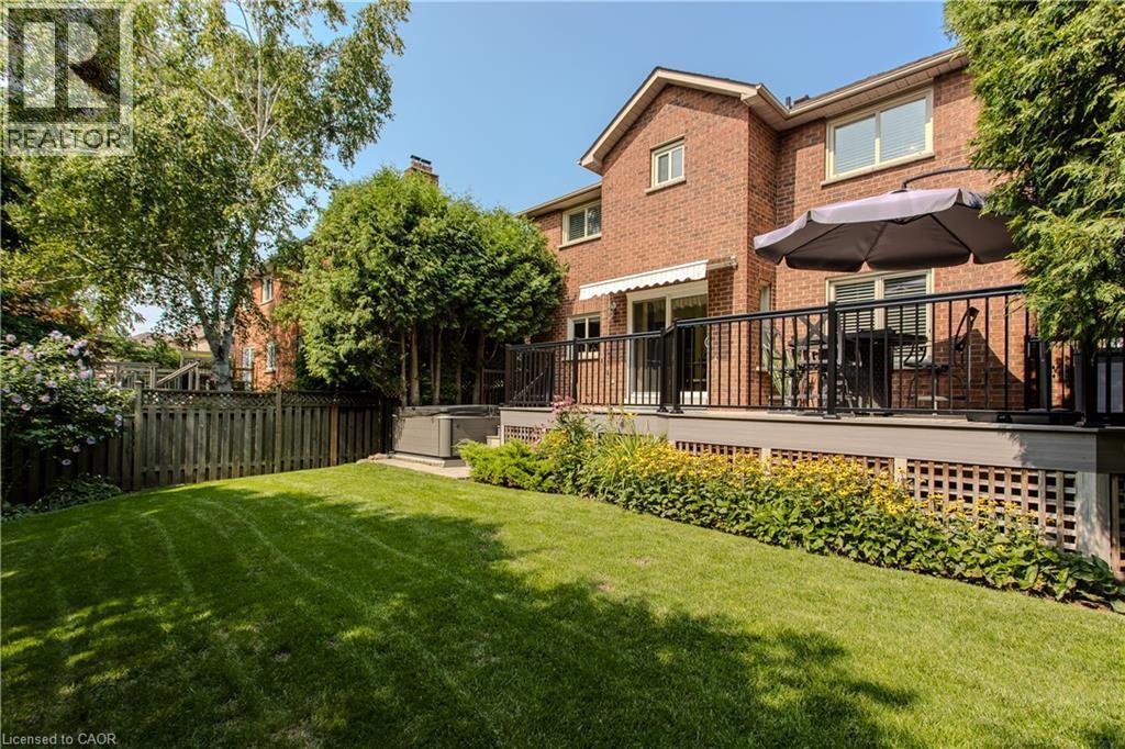 Brick exterior residence featuring a deck with black railings, a wooden privacy fence, a lawn, and mature trees - 1238 Sable Drive, Burlington, ON - Outdoor With Deck Patio Veranda