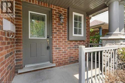 Brick facade with a covered entry, featuring a decorative glass panel door, a porch light fixture, and a window with white blinds - 76 Renner Drive, Cambridge, ON - Outdoor With Deck Patio Veranda With Exterior