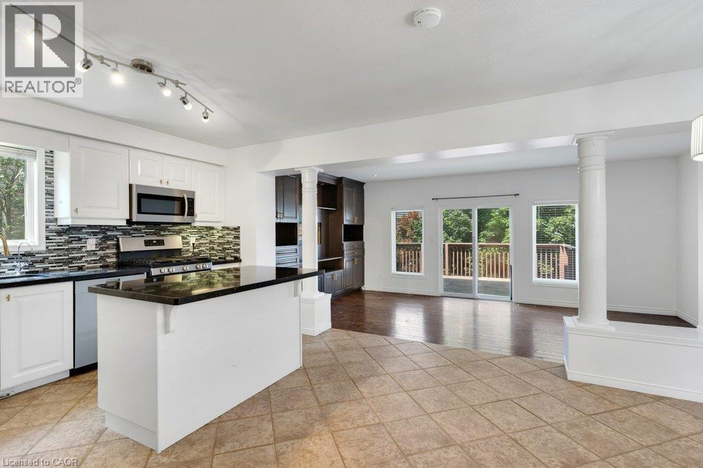 Open concept kitchen featuring white cabinetry, black countertops, stainless steel appliances, and a tiled backsplash - 76 Renner Drive, Cambridge, ON - Indoor Photo Showing Kitchen With Upgraded Kitchen