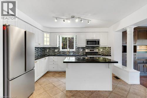 Kitchen featuring white cabinetry, dark countertops, stainless steel appliances, a tiled backsplash, and an island with a breakfast bar - 76 Renner Drive, Cambridge, ON - Indoor Photo Showing Kitchen